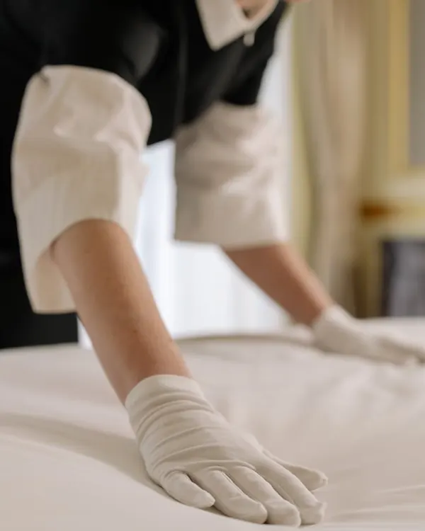 Housekeeping in white gloves smoothing the sheets on a hotel bed