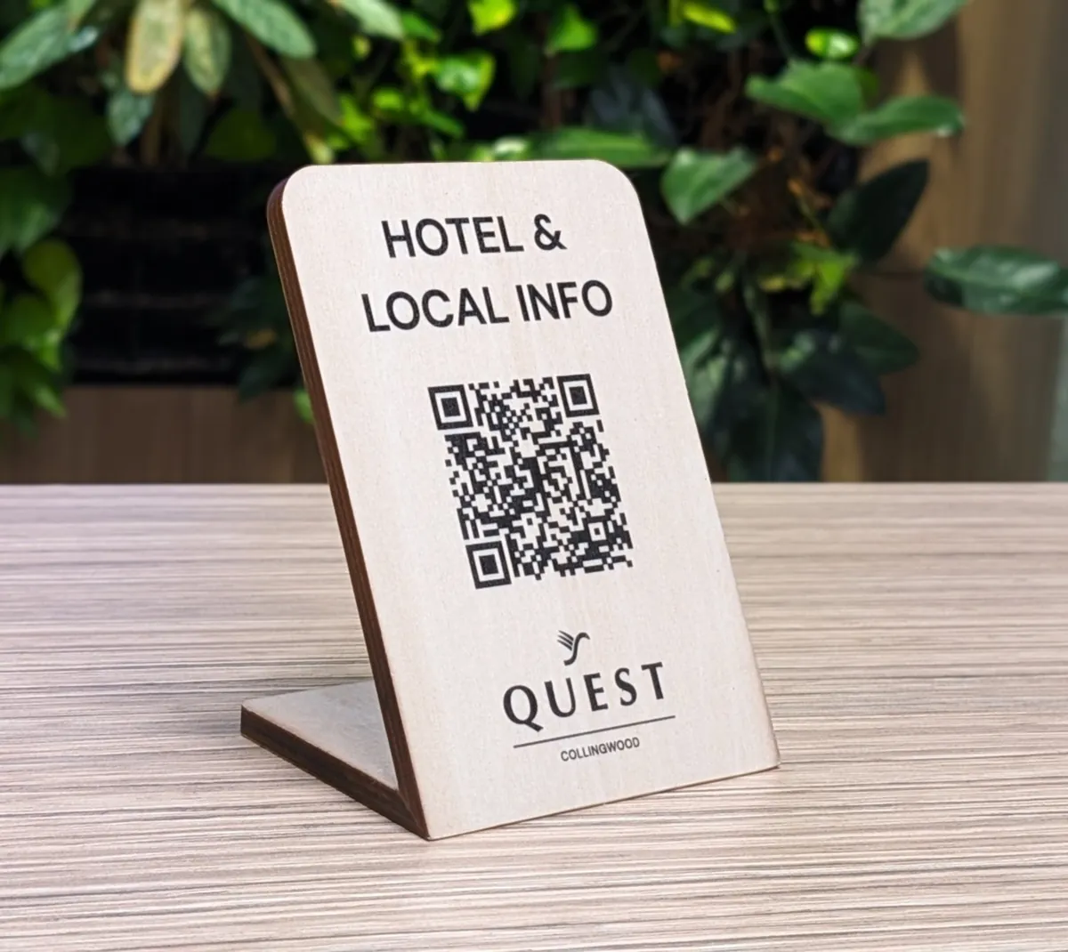 A wooden “Hotel & local info” QR stand for Quest Collingwood on a desk
